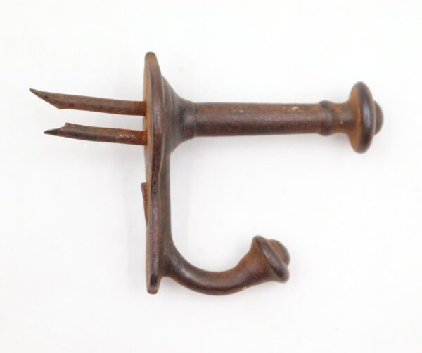 Cast iron wall hook with two pointed tack ends and a curved lower arm, shown in close-up with rusted surface wear.