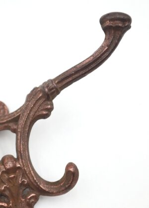 Close-up of a Victorian wall hook with a copper finish and ornate cast iron scrollwork.