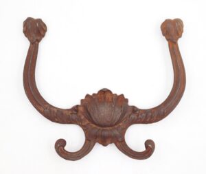 Victorian cast iron hall tree hook with a four-prong design and ornate floral center, shown front on with a heavily rusted surface and curved hooks at the bottom.