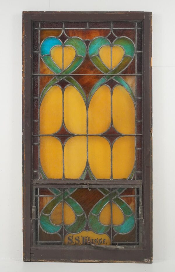 Rectangular stained glass church window with yellow, amber, brown, and blue leaded panels in a worn reddish-brown wood frame, shown with a lower section protected by acrylic.