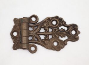 Antique Victorian brass ice box hinge with ornate scrollwork and four mounting holes, shown in a side view with a patina finish.