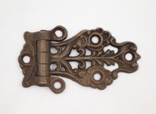 Antique Victorian brass ice box hinge with ornate scrollwork and four mounting holes, shown in a side view with a patina finish.