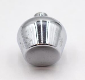 Close-up of a chrome-finished brass cabinet knob with a concave tulip shape and visible surface wear, shown from the front with the mounting screw partly visible at the top.