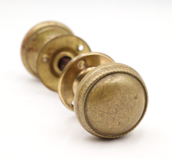 Traditional brass door knob set with a beaded edge, shown in close-up with one knob, rosette, and spindle visible, featuring worn surface wear and an antique brass finish.