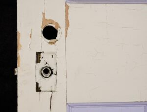 Close-up of a painted wood privacy door showing the latch edge, a circular hole for privacy hardware, and chipped paint with surface wear.
