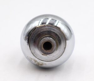 Close-up of a chrome-finished cabinet knob with a concave center and visible mounting hole, shown from the back with surface wear.