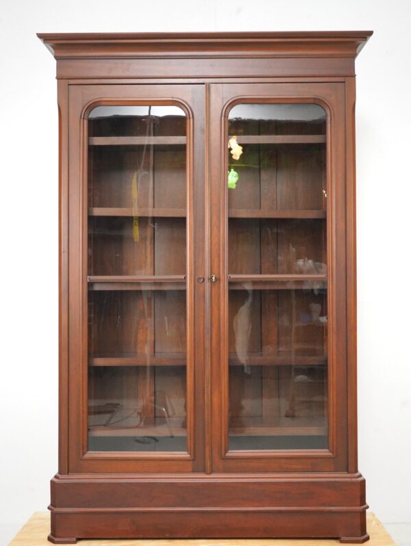 Front view of walnut bookcase with glass doors and shelves, highlighting wood grain and clear shelving.