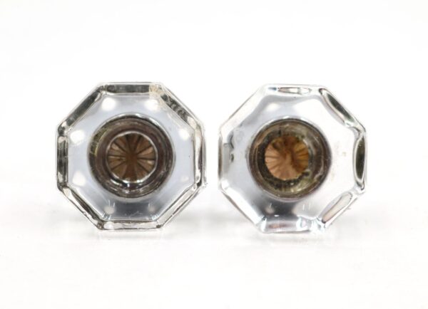 Pair of clear octagon glass cabinet knobs shown side by side, each with a chrome-plated brass shank and visible wear from use.