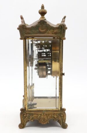 Front view of the Regulator clock highlighting brass and glass case, with clockwork and ornate finial visible against a white background.