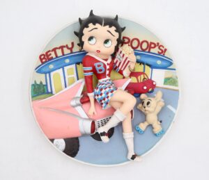 3-D sculptural collector plate showing Betty Boop sitting on a pink car at a drive-in with her dog Pudgy and a popcorn box.