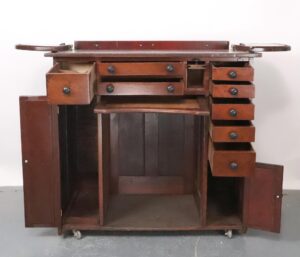 Front view showing all drawers and side doors open, revealing internal compartments and central open section on rolling base. Angled view focusing on left side doors opened wide, highlighting the worn finish and unique drawer arrangement. Close-up of upper small drawers partially pulled out, detailing handles and wood texture with visible aged patina. Side view displaying wheels beneath the cabinet and both large side doors swung outward for full interior access. Detail shot of central open section surrounded by closed drawers, illustrating the contrast in wood wear.