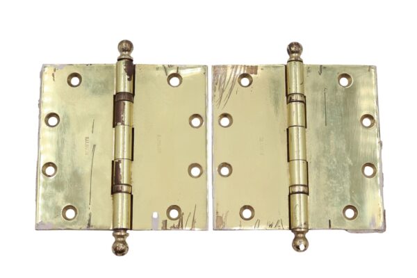 Pair of polished brass door hinges with ball tips, shown as a matching pair with five knuckles, template hole pattern, and visible surface wear.