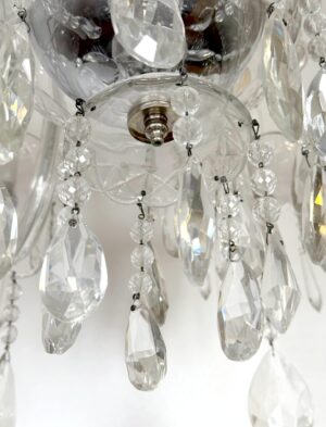 Close-up of a clear crystal chandelier with hanging teardrop and round prisms around a metal ceiling mount.