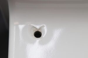 Close-up of a white ceramic bathroom shelf showing one predrilled drainage hole and surface wear around the opening.