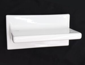 White ceramic bathroom shelf shown in a close-up side angle, with a rectangular form, a protruding front ledge, and a glossy porcelain finish visible on the surface.