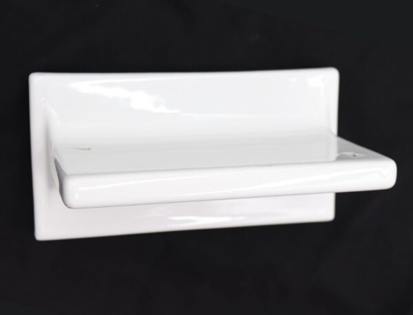 White ceramic bathroom shelf shown in a close-up side angle, with a rectangular form, a protruding front ledge, and a glossy porcelain finish visible on the surface.