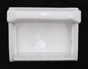 White ceramic soap dish with a handle, shown front on with a rectangular recessed center and slight surface wear along the edges.
