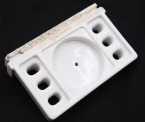 White ceramic bathroom holder with a central cup recess, three toothbrush holes on each side, and visible surface wear along one edge.