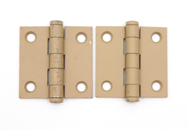 Pair of tan steel cabinet door hinges shown side by side, each with five knuckles and four mounting holes, with visible surface wear and chipped paint.
