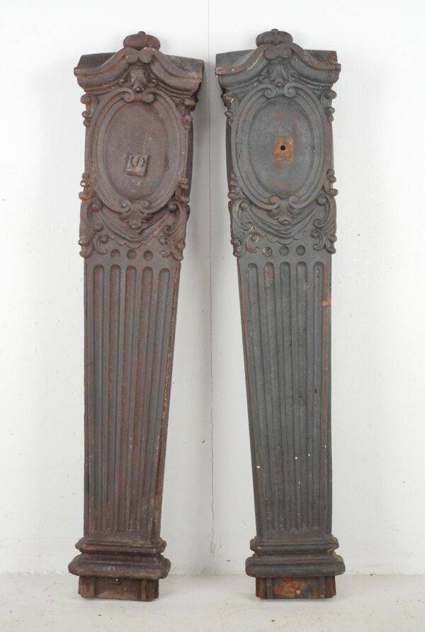 Pair of Victorian cast iron pilasters shown side by side, with ornate tops, fluted lower sections, and heavy surface wear and rust visible on both pieces.