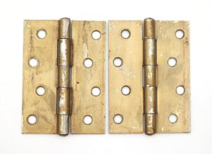 Pair of brass-plated cabinet door hinges shown side by side, each with five knuckles, a staggered hole pattern, and visible surface wear from prior use.