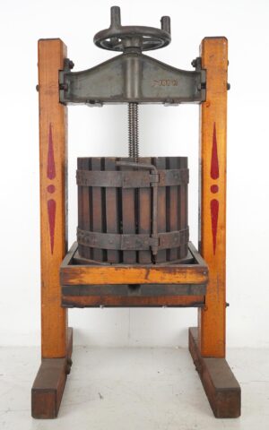 Antique fruit press with a dark wood stave barrel, metal bands, and a hand wheel mounted in a wooden frame with red painted accents.