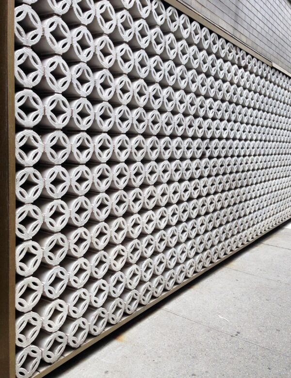Stacked white terra cotta wall bricks with round cutout faces shown in a long repeating facade pattern.