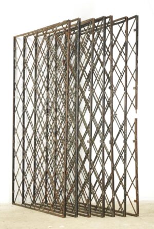 Set of seven industrial steel security panels with a diamond mesh pattern and rectangular frames, shown stacked together with surface wear, rust, and slight warping visible on the black finish.