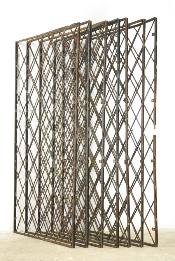 Set of seven industrial steel security panels with diamond mesh and rectangular frames, shown leaning together with visible surface wear, rust, and slight warping.
