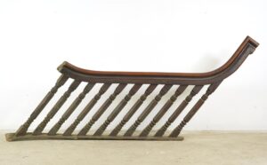 Antique stair railing set with a curved hand-carved banister and turned spindles in a dark wood tone, shown as a long single section.