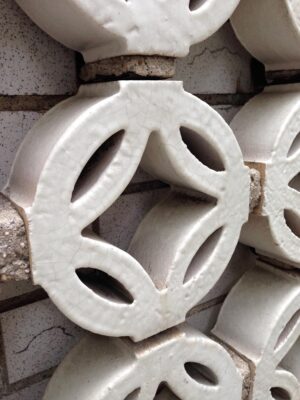 Close-up of a white terra cotta wall brick with a crackled glaze and oval cutouts in a stacked facade pattern.