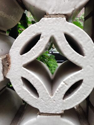 Close-up of a white terra cotta wall brick with a crackled glaze and four cutout openings.