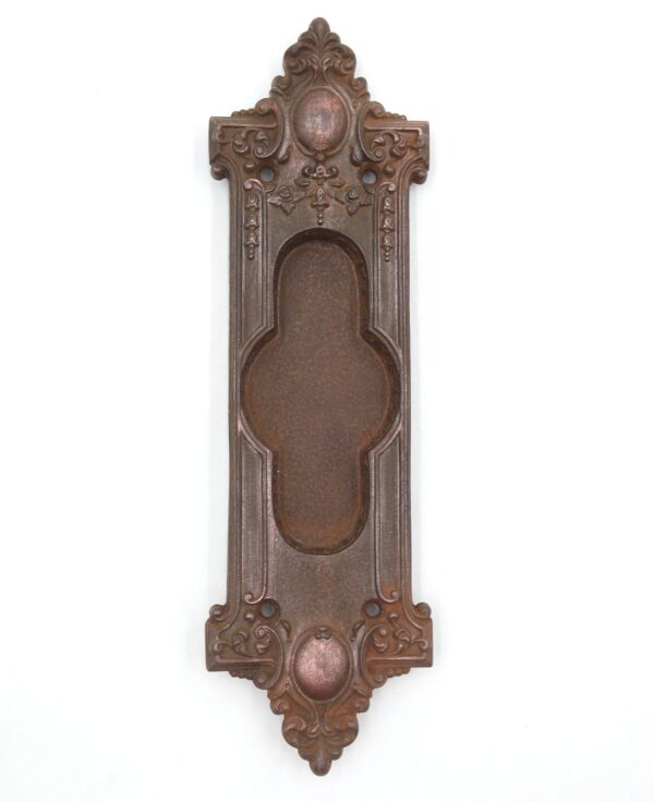 Victorian cast iron pocket door pull with an ornate recessed oval grip and mounting holes, shown front on.