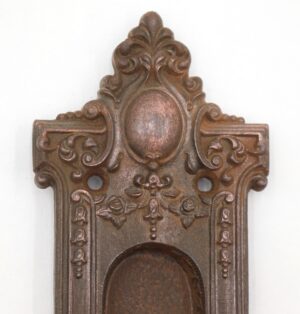 Victorian cast iron pocket door pull with ornate recessed plate, oval center, and two mounting holes.