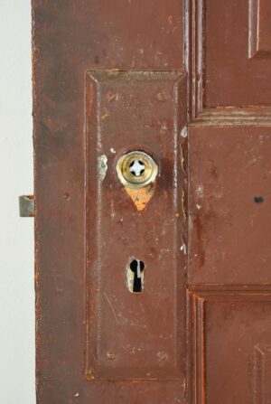 Close-up of a five-panel wood passage door showing the broken brass knob set and keyhole on the brown-painted side, with visible surface wear and chipped edges.