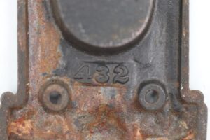 Close-up of an antique Victorian cast iron pocket door pull with a black finish, showing the recessed grip, mounting holes, and rusted surface wear.