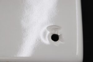 Close-up of a white ceramic bathroom shelf showing one predrilled drainage hole and a glossy surface with visible wear and chips.