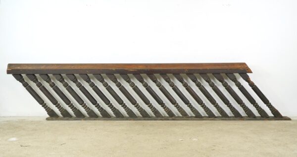 Antique stair railing set with a long dark wood banister and evenly spaced carved spindles shown in a side view.