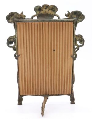 Art Nouveau bronze vanity mirror frame with an ornate scalloped top, a fluted backing panel, and visible surface wear.