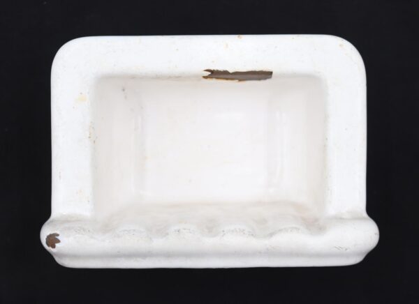 White enameled cast iron recessed soap dish with a rectangular shape and visible surface wear and enamel chips.