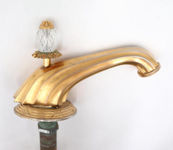 Empire bathroom faucet with a scalloped gilded brass spout, round ornate base, and clear cut glass pop-up drain.