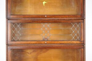 Close-up of a barrister bookcase with three stacked sections, including an etched glass door and brass knobs on dark wood framing.