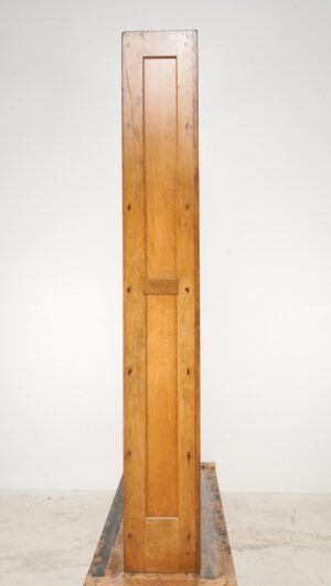 Tall wooden bookcase shown from the side, with a medium wood tone and visible surface wear.