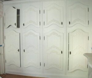 White built-in cabinet bank with eight paneled doors, four upper and four lower, shown partly open and fitted with original hardware.