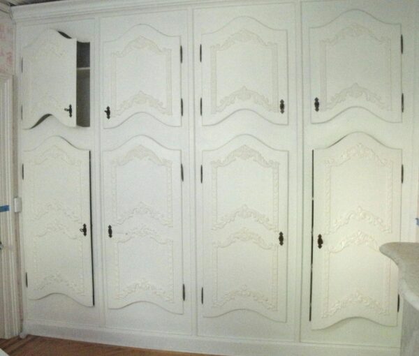 White built-in cabinet bank with eight paneled doors, four upper and four lower, shown partly open and fitted with original hardware.