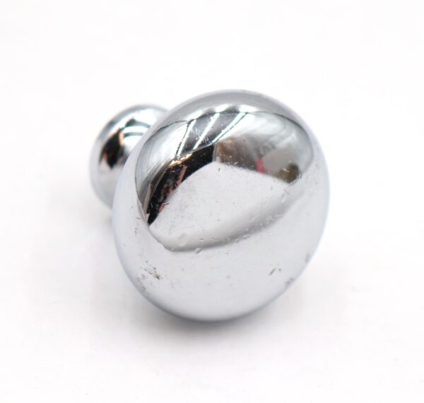 Chrome round cabinet knob shown in close-up, with a mounting screw visible behind it and light surface wear on the finish.