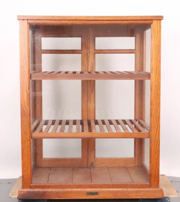 Antique countertop display cabinet with a glass front, two slatted shelves, and a mesh back.