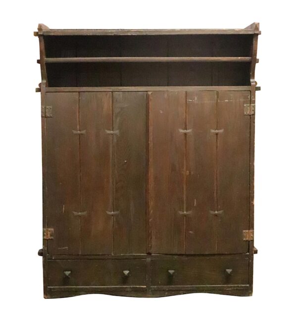 Front view of a dark wood tone oak storage cabinet with open upper shelves, two lower drawers, and paneled doors held by butterfly pegs.