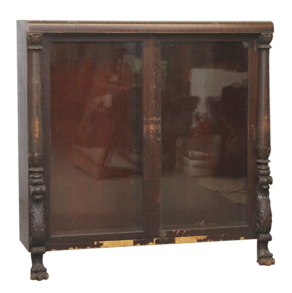Empire style wooden cabinet with glass double doors, carved columns, and front claw feet.