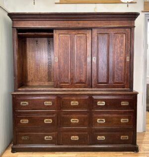 Dark wood cabinet with two sliding doors, an open upper storage section with hooks, and nine drawers with recessed brass hardware.